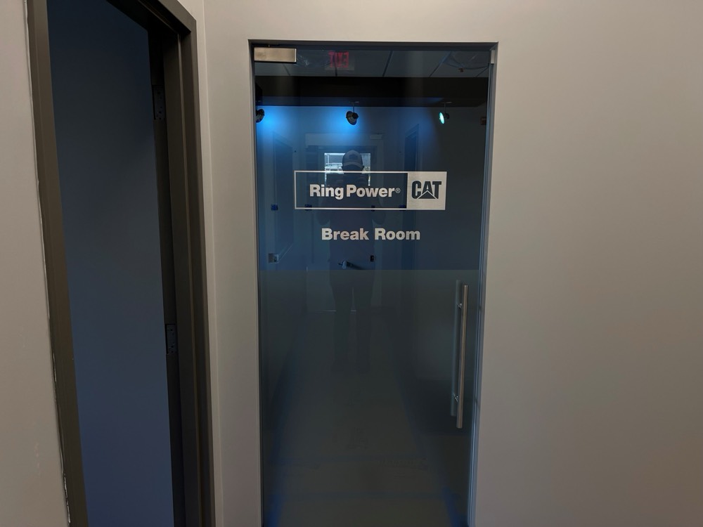 Frameless glass break room door with etched Ring Power CAT graphics and silver ladder-pull hardware — Ring Power CAT, Orlando FL